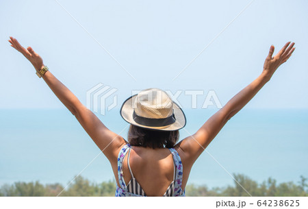 The image behind Asian women raise their arms and wear a hat  background sea. 64238625