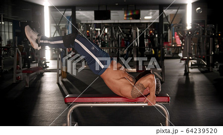 An adult man bodybuilder training his back and stamina in the gym lying on the bench 64239520