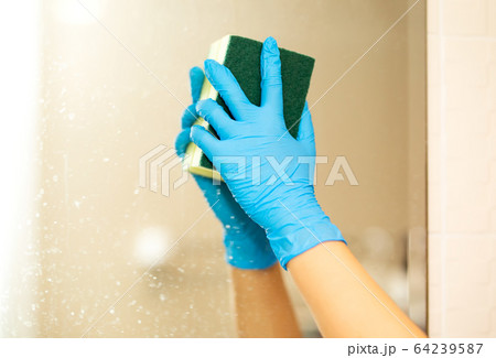 Women hand in a blue rubber glove in the picture, removes and washes bathroom sink by spray and sponge, hygiene concept 64239587