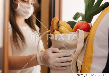 Delivery man in mask and gloves give fresh food to recipient and young woman customer. Stay home, Online shopping concept 64252547