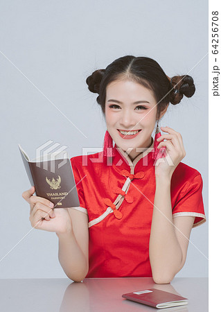Happy asian woman in chinese dress traditional holding passport in hand on grey background; Portrait beautiful girl in the Cheongsam red dress look at the camera in studio; Happy new year concept. Happy asian woman in chinese dress traditional holding passport in hand on grey background; Portrait beautiful girl in the Cheongsam red dress look at the camera in studio; Happy new year concept. 64256708