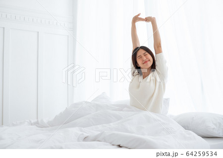 Asian woman wake up in the morning, sitting on white bed and stretching, feeling happy and fresh Asian woman wake up in the morning, sitting on white bed and stretching, feeling happy and fresh 64259534