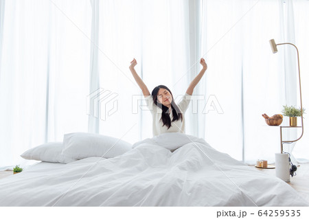 Asian woman wake up in the morning, sitting on white bed and stretching, feeling happy and fresh Asian woman wake up in the morning, sitting on white bed and stretching, feeling happy and fresh 64259535