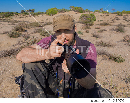 Close up pictire of a ohotographer in savanna taking a picture of a wild life of an animals. Close up pictire of a ohotographer in savanna taking a picture of a wild life of an animals. 64259794