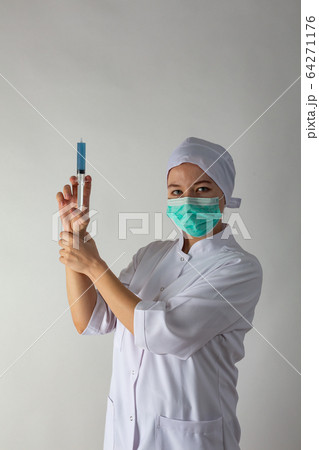 The girl in a medical coat holds a large syringe with blue liquid like a gun 64271176