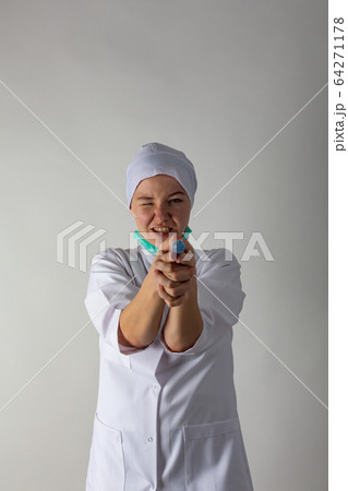 The girl in a medical coat holds a large syringe with blue liquid like a gun 64271178