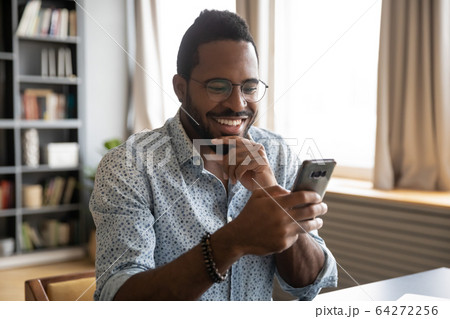 Smiling millennial biracial guy reading pleasant good news sms. Smiling millennial biracial guy reading pleasant good news sms. 64272256