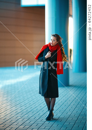 Young beautiful girl with perfect make-up, red lips, wearing a dark coat, red shirt, posing near shopping center. She just got out of high-end clothing store Young beautiful girl with perfect make-up, red lips, wearing a dark coat, red shirt, posing near shopping center. She just got out of high-end clothing store 64272452