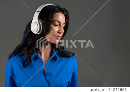 Attractive european adult woman with long hair dancing with headphones on grey studio background 64273608