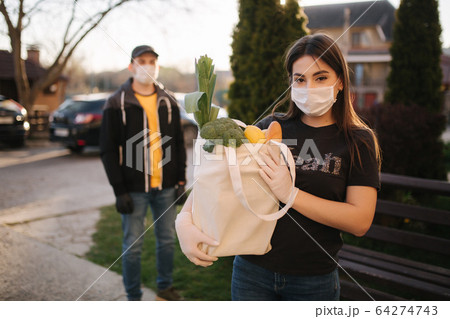 Courier in protective mask and medical gloves delivers fresh food for female customer. Delivery service under quarantine. Coronavirus covid-19 theme Courier in protective mask and medical gloves delivers fresh food for female customer. Delivery service under quarantine. Coronavirus covid-19 theme 64274743