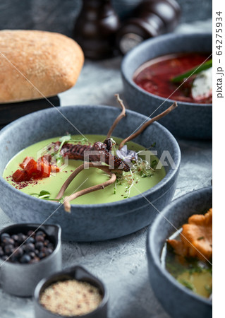 Gray plates with different soups on a gray background. Plate with asparagus soup with octopus, a plate of traditional borscht with sour cream, a plate with mushroom soup and standing on multi-colored 64275934