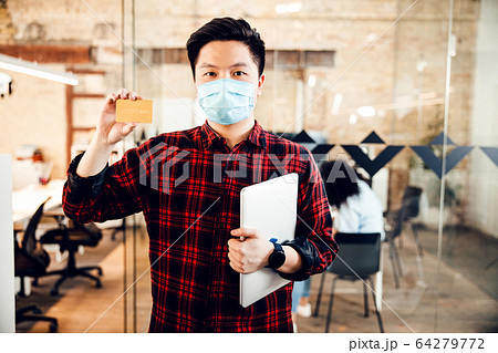 Handsome young man in medical face mask holding gold card Handsome young man in medical face mask holding gold card 64279772