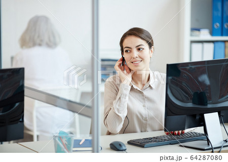 Smiling Female Secretary Wearing Headset at Workplace 64287080