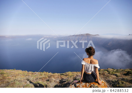 A young woman sits on the edge of a mountain and enjoys the view 64288532