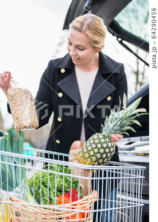 Woman storing basket with groceries into trunk after shopping 64290456