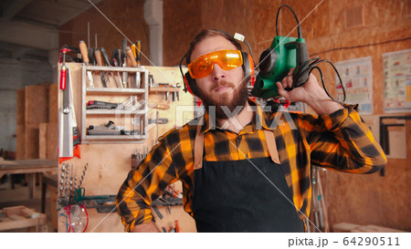 Bearded man worker in yellow shirt standing in the workshop - holding grinding instrument 64290511