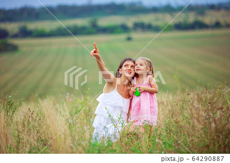 Happy mother and daughter spending time together outdoors, pointing fingers and enthusiastically looking up, with pleasure spending time in countryside Happy mother and daughter spending time together outdoors, pointing fingers and enthusiastically looking up, with pleasure spending time in countryside 64290887