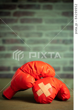 Red boxing gloves on wooden table and brick wall at the sport gym. Adhesive plaster across each other on boxing gloves. Idea of getting hurt or combat losing business rival. Fighting giving up boxing Red boxing gloves on wooden table and brick wall at the sport gym. Adhesive plaster across each other on boxing gloves. Idea of getting hurt or combat losing business rival. Fighting giving up boxing 64299952
