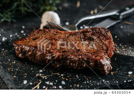 Grilled sirloin steak on the black marble plate seasoned with condiments 64303054