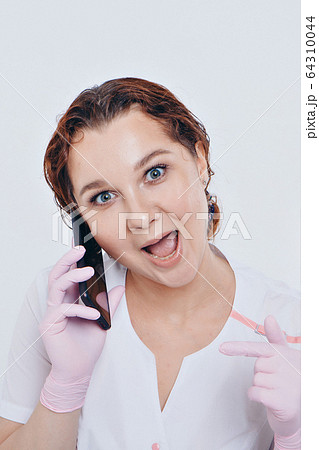 a doctor in gloves is talking on the phone on a white background. A woman learns the techniques of business planning, quarantine, self-isolation, protection from coronavirus, virus, remote work. 64310044