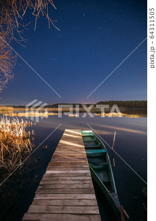Belarus, Eastern Europe. Real Night Sky Stars Above Old Pier With Moored Wooden Fishing Boat. Natural Starry Sky And Countryside Landscape With Lake River In Early Spring Night. Russian Nature 64311505