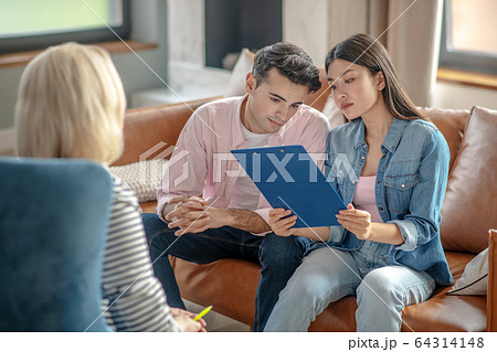 Dark-haired tall man sitting next to his girlfriend reading something Dark-haired tall man sitting next to his girlfriend reading something 64314148