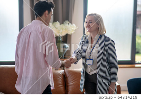 Blond psychologist greeting her young male patient in her office and smiling Blond psychologist greeting her young male patient in her office and smiling 64314219