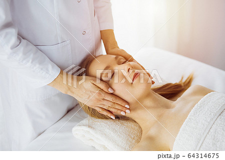 Beautiful caucasian woman enjoying facial massage with closed eyes in spa salon. Relaxing treatment in medicine and Beauty concept Beautiful caucasian woman enjoying facial massage with closed eyes in spa salon. Relaxing treatment in medicine and Beauty concept 64314675