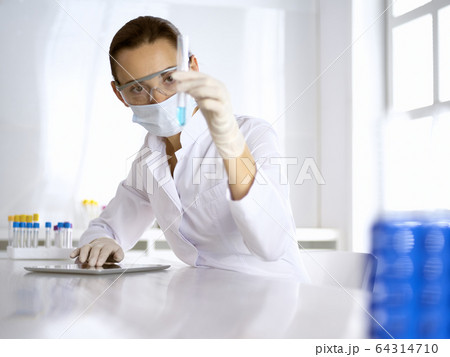 Female laboratory assistant in mask analyzing test tube with blue liquid. Medicine, health care and virus pandemic protection 64314710