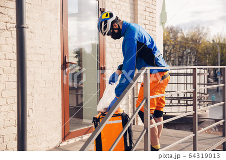 Contacless delivery service during quarantine. Man delivers food and shopping bags during isolation 64319013