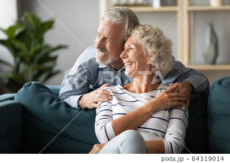 Smiling older couple dreaming together, looking out window Smiling older couple dreaming together, looking out window 64319014