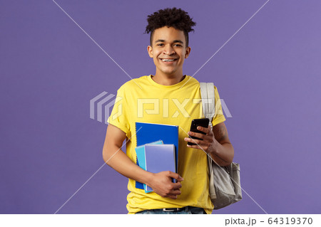 Back to school, university concept. Portrait of cheerful young handsome male student wearing backpack on shoulder, hold notebooks and studying books, texting friend mobile phone Back to school, university concept. Portrait of cheerful young handsome male student wearing backpack on shoulder, hold notebooks and studying books, texting friend mobile phone 64319370