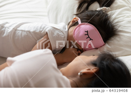 Small girl wears sleeping eyemask lying in bed with mother 64319408