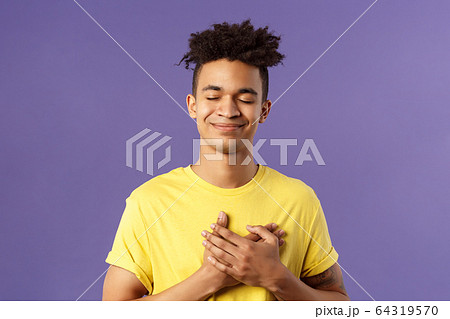 Always in my heart. Touched, carefree handsome young man with dreads, yellow t-shirt, close eyes and smiling, hold hand on chest as recall memory of his first love, feel heartwarming emotion Always in my heart. Touched, carefree handsome young man with dreads, yellow t-shirt, close eyes and smiling, hold hand on chest as recall memory of his first love, feel heartwarming emotion 64319570