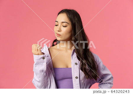 Close-up portrait of arrogant stylish young asian girl not listening, feeling careless and uninterested in conversation, bored looking at hand, thinking visit nails studio, pink background 64320243