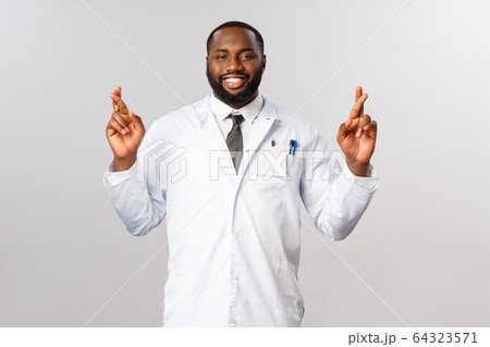 Coronavirus, covid19 and healthcare concept. Hopeful optimistic african-american doctor having faith in nations infectionists working on corona vaccine, cross fingers praying for good luck 64323571