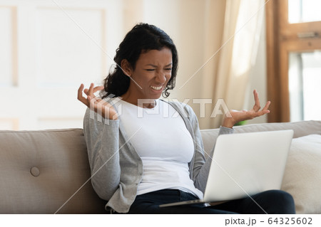 Annoyed young black girl looking at laptop screen Annoyed young black girl looking at laptop screen 64325602