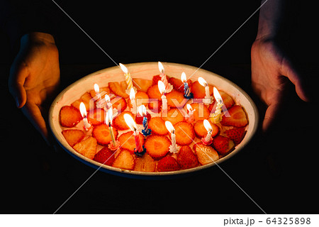 Hands of woman hold a homemade strawberry cake with lit birthday candles 64325898