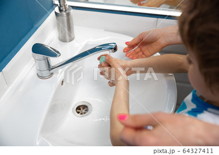 Mother washing hands her son carefully in bathroom close up. Prevention of infection and pneumonia virus spreading Mother washing hands her son carefully in bathroom close up. Prevention of infection and pneumonia virus spreading 64327411