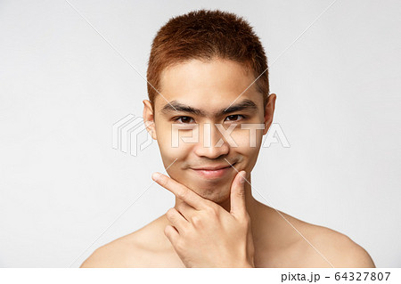 Beauty, skincare and men health concept. Headshot of smart and creative asian young man standing naked torso, look pleased, touch chin and smiling camera, have idea, thinking-up plan 64327807