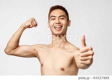 Workout, lifestyle and health concept. Portrait of proud, boastful handsome asian man flex biceps, become strong in gym, show thumb-up, recommend training program, smile plesaed Workout, lifestyle and health concept. Portrait of proud, boastful handsome asian man flex biceps, become strong in gym, show thumb-up, recommend training program, smile plesaed 64327889