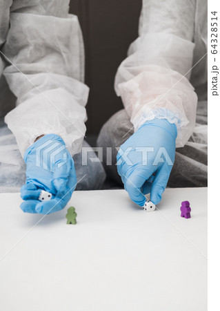 Two people in protective white translucent suit, blue rubber gloves, medical mask sit on sofa at home and play board games, roll dice. Stay home during coronavirus pandemic covid. 64328514