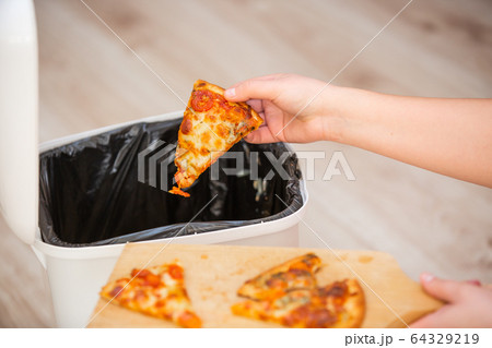 Stop wasting food, Woman hand throwing some food, pizza pieces to the bin, trash, food concept Stop wasting food, Woman hand throwing some food, pizza pieces to the bin, trash, food concept 64329219