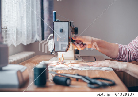 Woman sewing medical masks on sewing machine during coronavirus pandemic, protection against covid-2019, homemade sewing Woman sewing medical masks on sewing machine during coronavirus pandemic, protection against covid-2019, homemade sewing 64329237