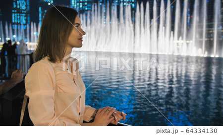 Girl tourist watches the fountains in Dubai in the evening. 64334130