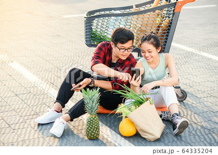 Attractive vietnamese boy and beauiful girl sitting on the parking near shopping mall and uses their smartphones. Attractive vietnamese boy and beauiful girl sitting on the parking near shopping mall and uses their smartphones. 64335204