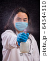 Young heath worker spraying disinfectant solution to the camera as she wears face mask  64344310