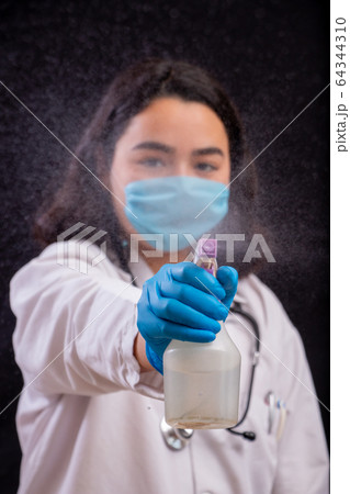 Young heath worker spraying disinfectant solution to the camera as she wears face mask  64344310