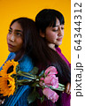 Two latin young ladies posing back to back, yellow background, roses and sunflowers 64344312