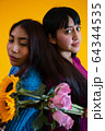 Two latin young ladies posing back to back, yellow background, roses and sunflowers 64344535